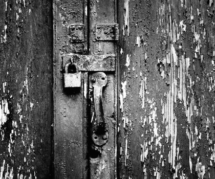 Rusty, unused lock on an old wooden door with peeling paint.