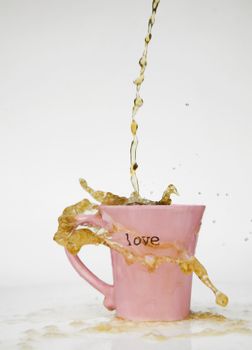 Coffee splashes over the rim of a pink cup with the word "love" on it.