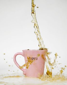 Coffee splashes over the rim of a pink cup with the word "love" on it.