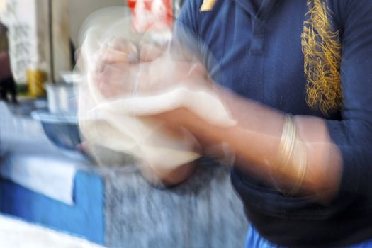 Motion blur of swift hands of a chef making a naan Indian flat bread in a Jammu Kashmir roadside hut of Northern Indian at the foothills of the Himalayas. Horizontal landscape with crop margins and copy space
