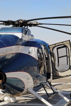 Portrait of blue metallic and white small helicopter abstract with open right hand door stationed on a heliport