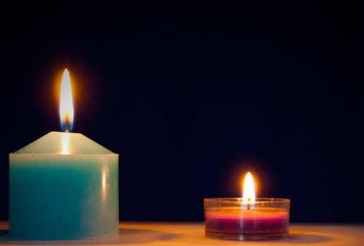 Two burning candles against dark blue background