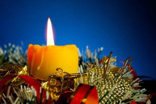 Burning candle with Christmas decorations against blue background