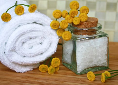 White bath towel, bottle of sea salt and yellow camomiles in spa composition