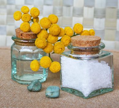 Bottles of essential oil and sea salt with yellow camomiles in spa composition 