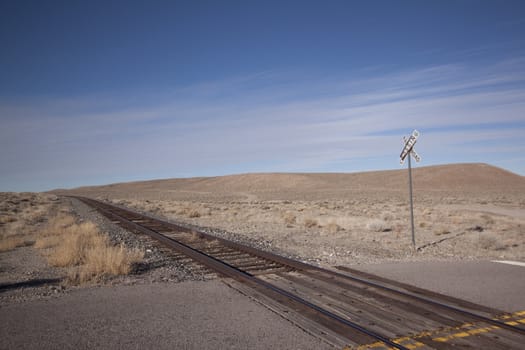 Railroad crossing tracks in the desert with blue skies.