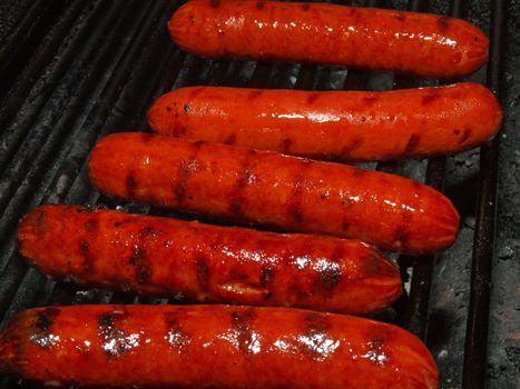A row of five hotdogs on a bbq grill