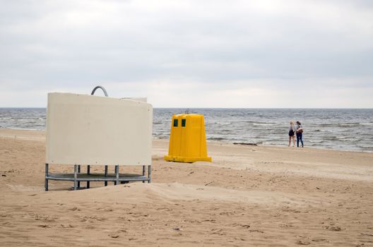 wear changing cabin, yellow waste bin container and couple pair young women walk on sea ocean beach coastline.