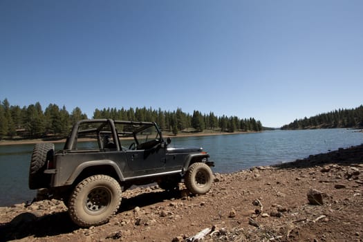a close up of offroad vehicle in the dirt. with a lake in the background