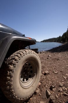 a close up of offroad tires in the dirt. with a lake in the background