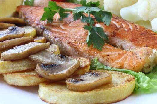 Fried salmon with potatoes, mushrooms, cauliflower and lemon on white plate