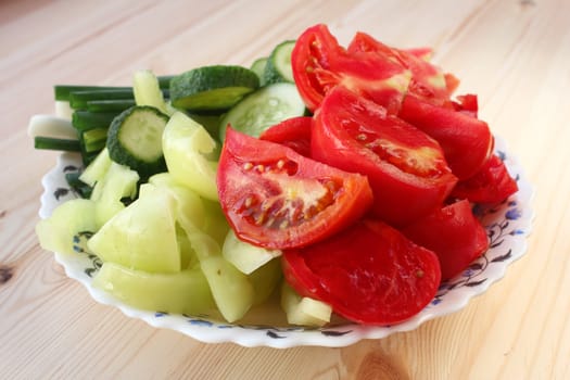 Fresh sliced tomatoes, pepper, cucumber and green onion in the plate on the wood table.