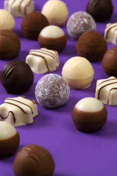 Photo of delicious white chocolates and truffles on purple table.
