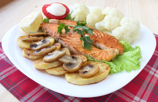 Fried salmon with potatoes, mushrooms, cauliflower, tomato and lemon on white plate