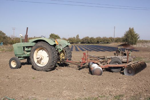 a farm tractor with a plow on the back with farm rows in the background.