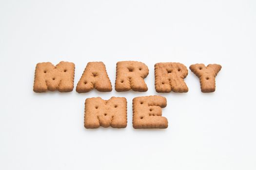 Words marry me arranged by brown biscuits on white background