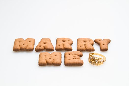 Word marry me arranged by brown biscuits with gold  ring on white background