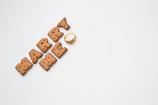 Word marry me arranged by brown biscuits with gold  ring on white background