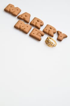 Angled view of the words marry me arranged by brown biscuits with gold ring on white background portrait orrientation