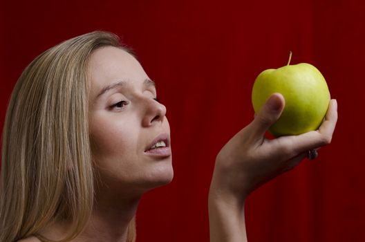 young blonde woman holding a green apple on red background