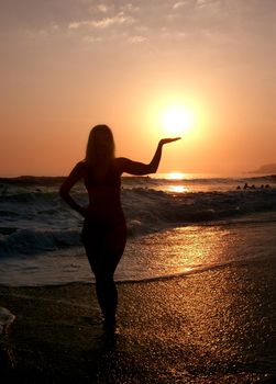 silhouette woman on beach holding sun in hand at sunset 