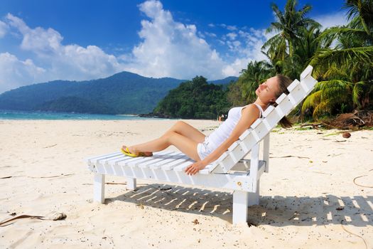 Girl on a tropical beach sitting at chaise lounge