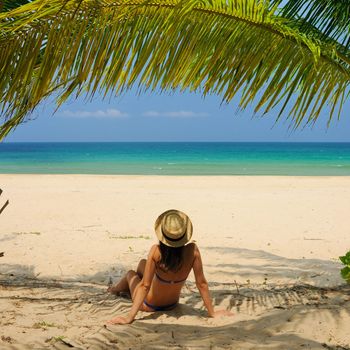 Woman at beach under palm tree with leaf shadow on her body