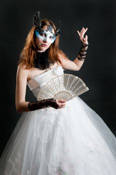 Girl with fan and mask in white dress on black background