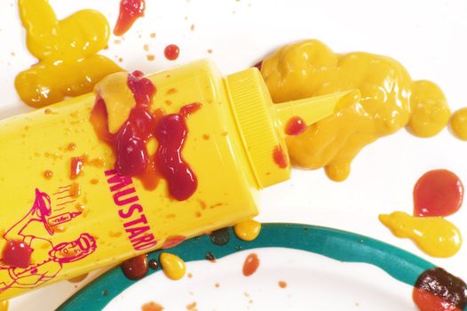 Mustard squeeze bottle and a mess of condiments on a plate.
