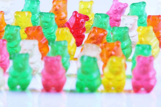 Colorful gummy bears lined up in rows, with the sole red bear being main focus. Isolated on white.;