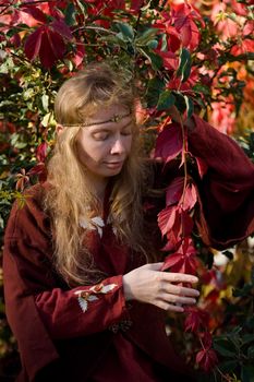 The blonde girle in medieval red dress in the autumn forest
