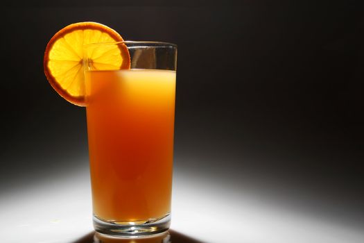 A Backlit glass of orange juice with a slice of orange