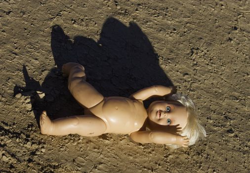Abandoned child's baby doll with blue eyes on parched desert dirt.