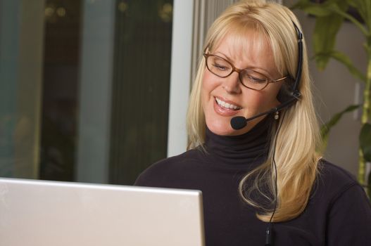 Attractive businesswoman smiles as she talks on her phone headset.