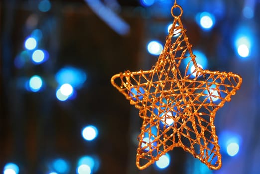 Gold star ornament with Christmas lights in background.