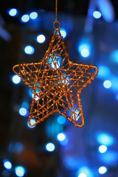 Gold star ornament with Christmas lights in background.