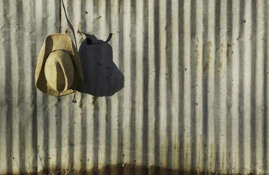 Straw cowboy hat hanging in front of old corrugated metal.