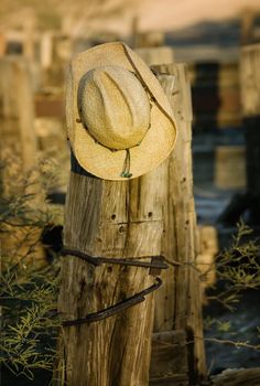 Straw cowboy hat hanging on an old wooden post.
