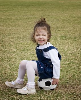 Little girl on a playground sitting on a soccer ball and making a funny face.