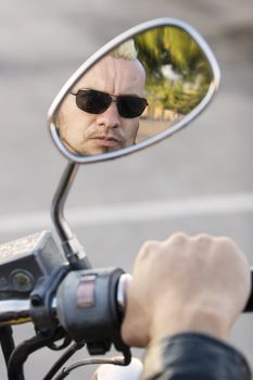 Man with a punk haircut seen in the rearview mirror of his motorcycle.