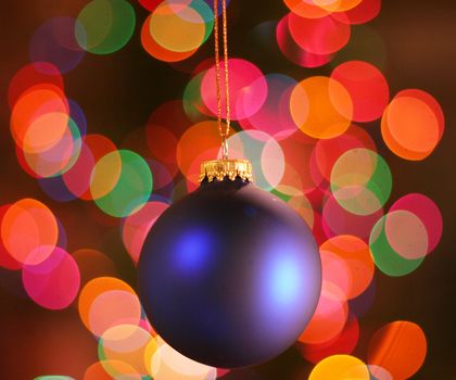 Blue frosted Christmas ornament with colorful lights in background.