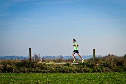 Male runner at sprinting speed training for marathon outdoors on country landscape.