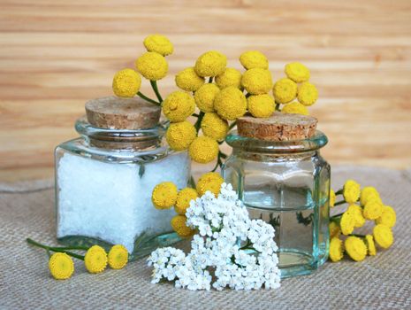 Bottles of essential oil and sea salt with yellow camomiles in spa composition
