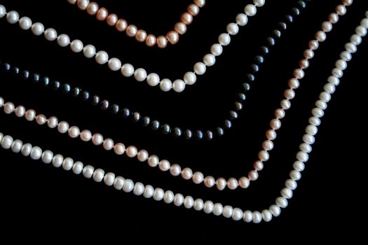 White, black and pink pearls on the black silk as background 