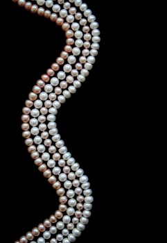 White, black and pink pearls on the black silk as background 