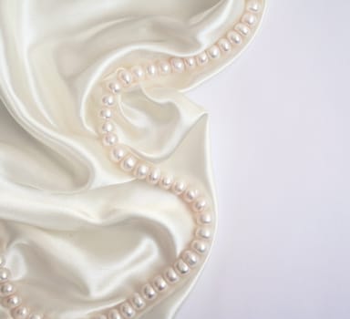 White pearls on the white silk as wedding background 