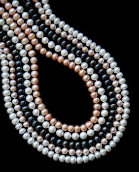 White, black and pink pearls on the black silk as background 