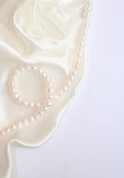 White pearls on the white silk as wedding background 