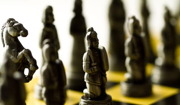 Silver chess set backlit on the checker board with bright background