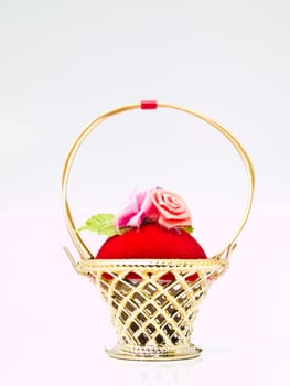 A miniature metalic wicker decorated by roses on a red velvet isolated on white background